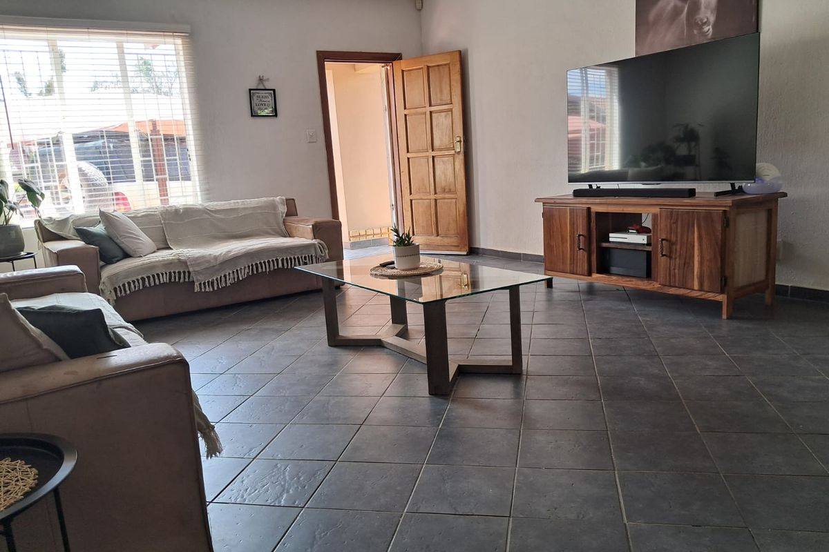 Spacious living room featuring dark tiled flooring, natural light through venetian blinds, and a solid timber door leading to an adjacent area.