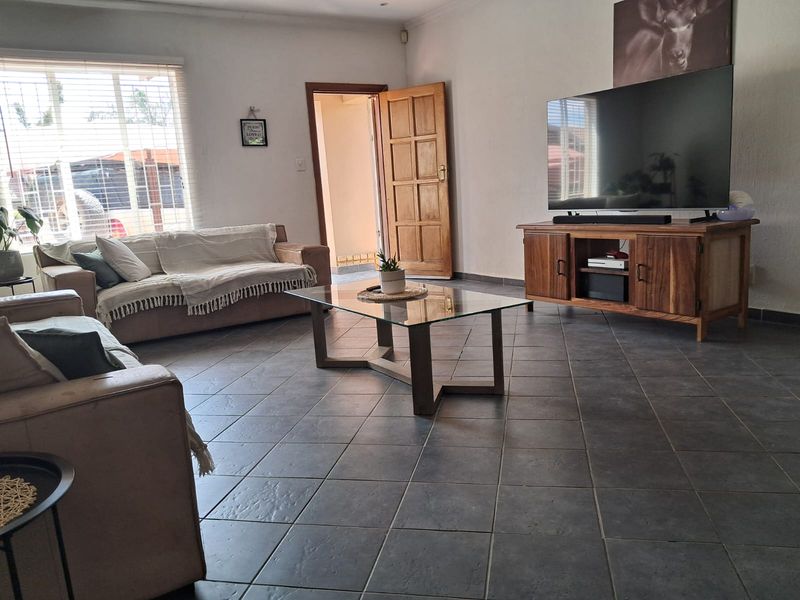 Spacious living room featuring dark tiled flooring, natural light through venetian blinds, and a solid timber door leading to an adjacent area.