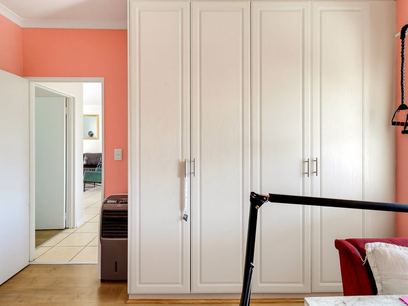 A bedroom featuring floor-to-ceiling built-in cupboards, laminate flooring, and a doorway leading to an adjacent living space.