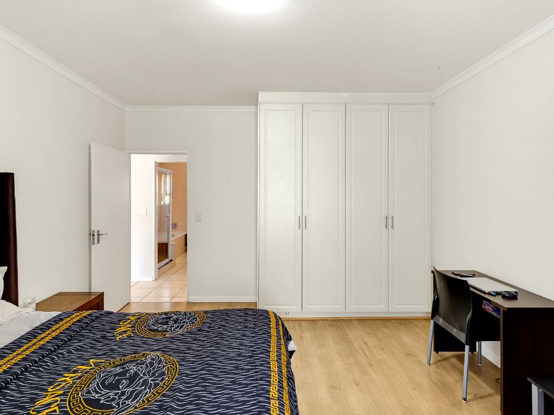 Spacious bedroom featuring light laminate flooring, built-in white cupboards, and direct access to an en-suite bathroom.