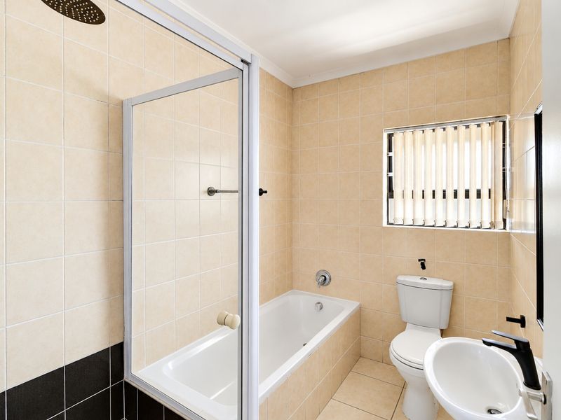 A functional bathroom featuring a combined shower and bathtub, a standard toilet, and a washbasin with tiled finishes throughout.