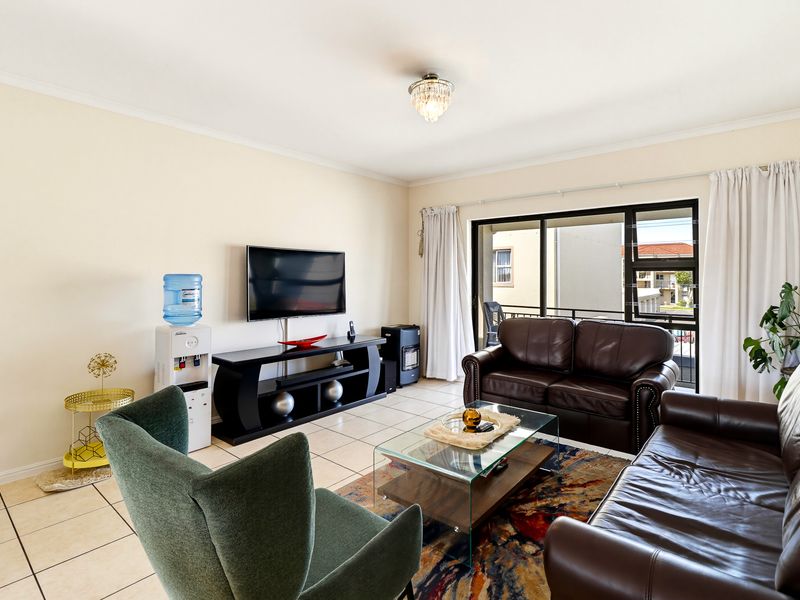 A bright living room featuring tiled flooring and a large sliding glass door providing access to the balcony.