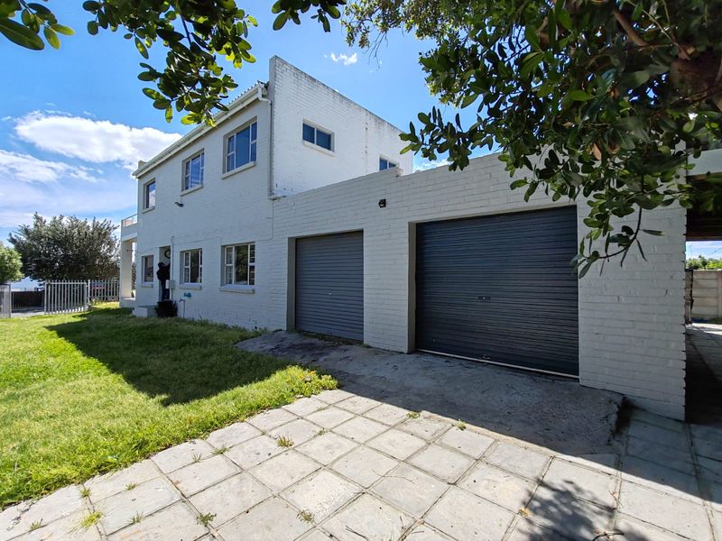Front view of a two-story house featuring a double garage with roller shutter doors, a paved driveway, and a lawn area.