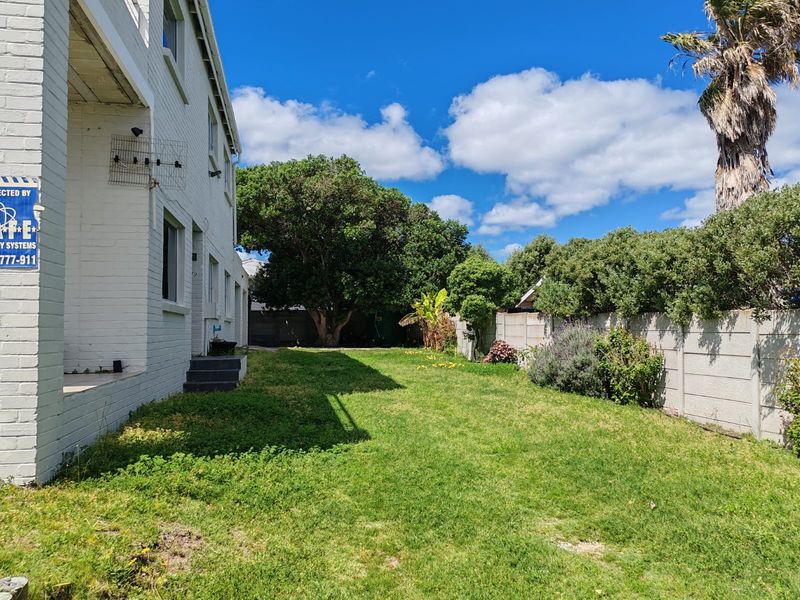 A rear garden view featuring a lawn area, mature trees, and a precast concrete boundary wall alongside the painted brick exterior of the house.