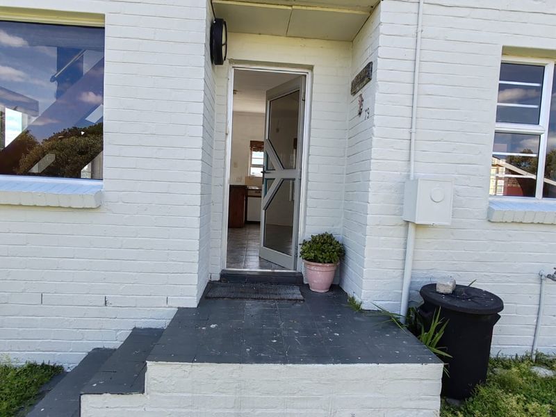 Front entrance of a white painted brick house featuring tiled steps and a security screen door, with visible access to the interior living space.