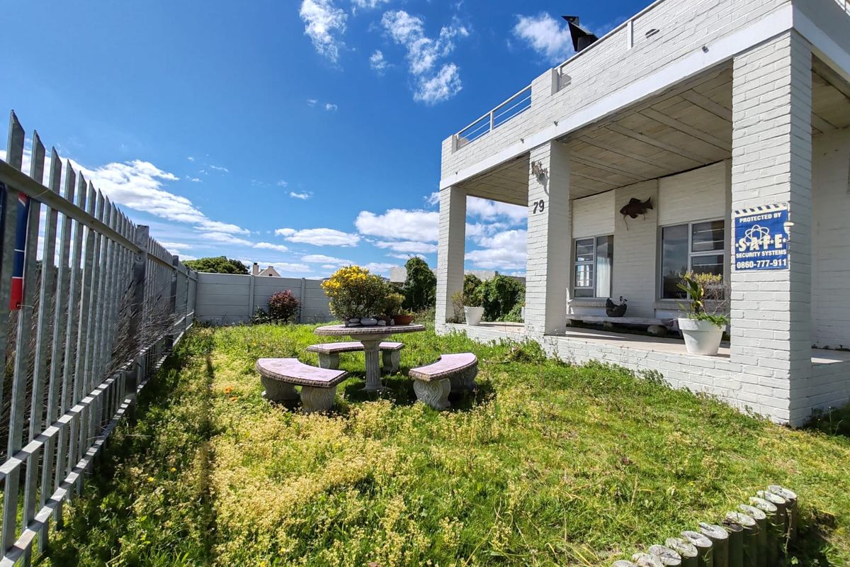 Rear exterior view of the property featuring a covered patio, balcony, and a large garden area enclosed by steel palisade and concrete walling.