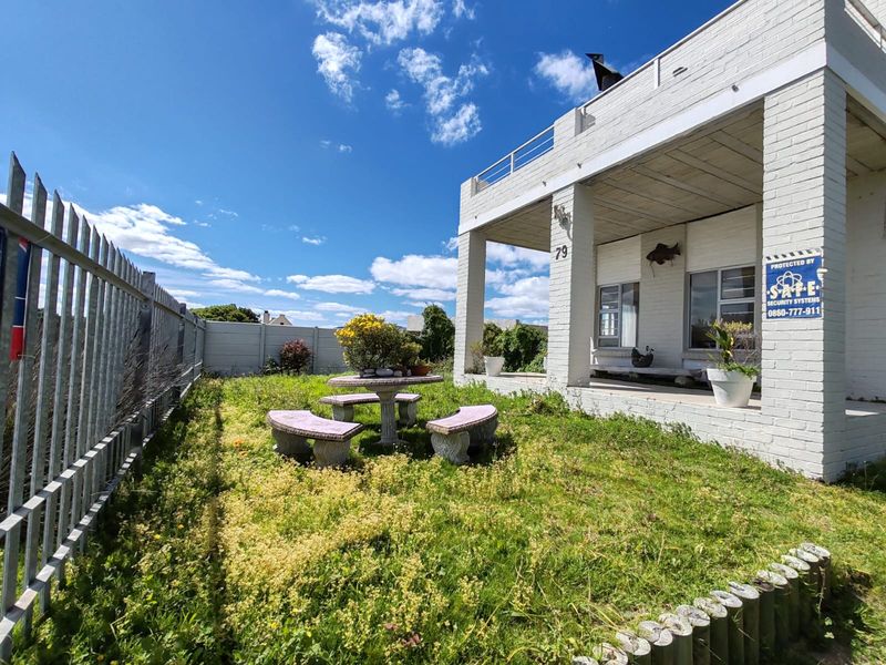 Rear exterior view of the property featuring a covered patio, balcony, and a large garden area enclosed by steel palisade and concrete walling.