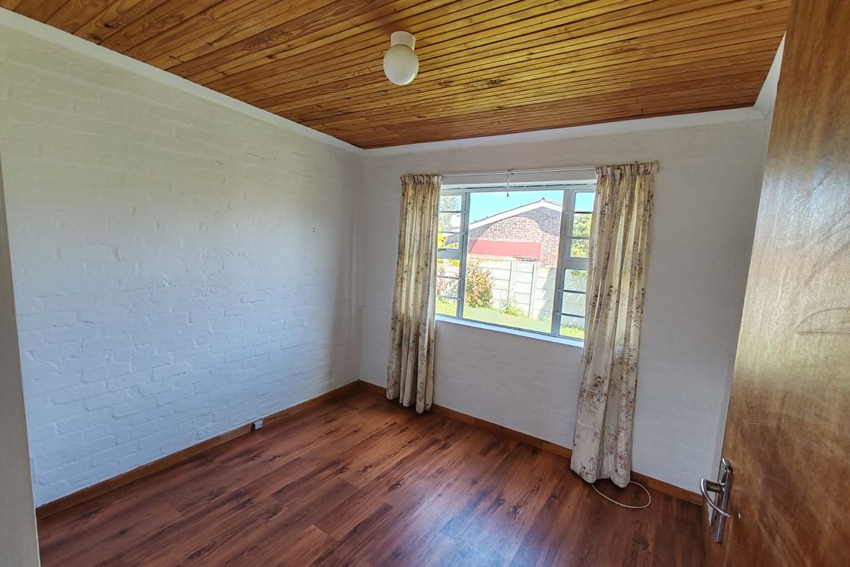 A bright, empty bedroom featuring warm timber ceiling paneling, laminate flooring, and painted brick walls, offering a clean canvas for personalization.