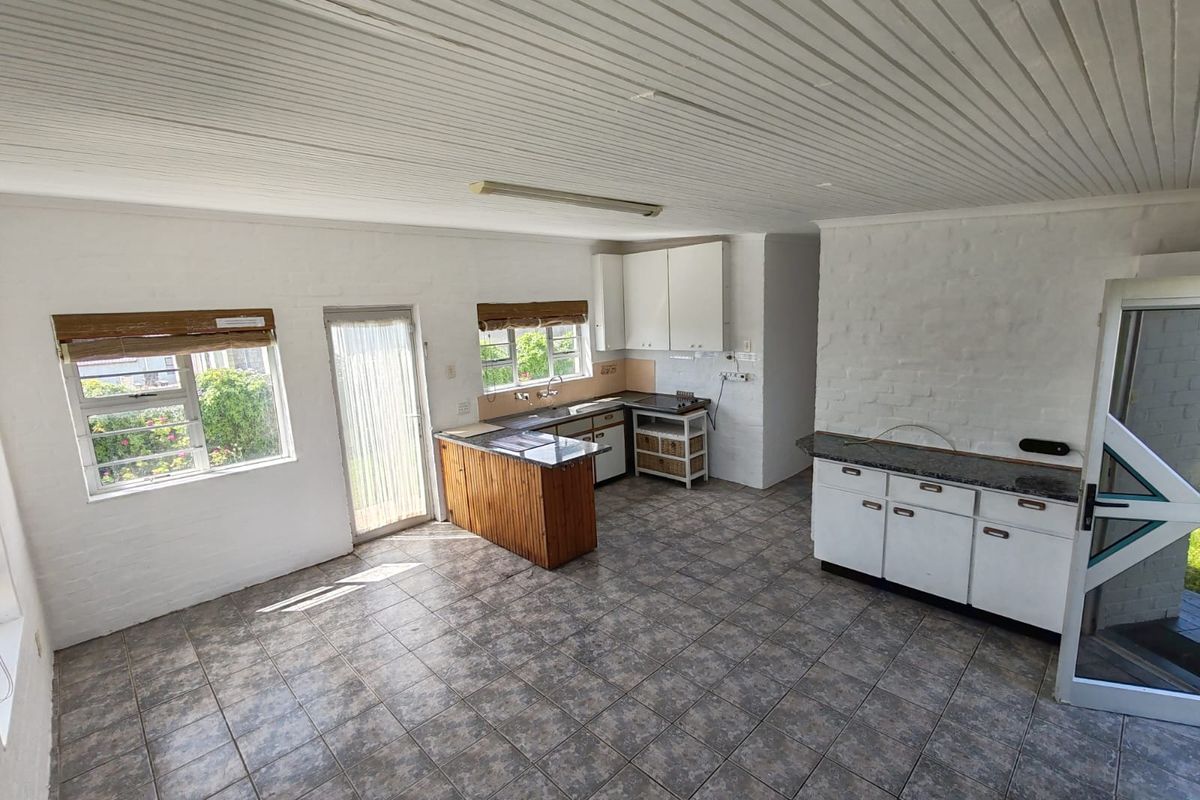 Spacious kitchen featuring tiled flooring, built-in cabinetry with stone countertops, and a timber-clad island, offering a functional layout with direct outdoor access.