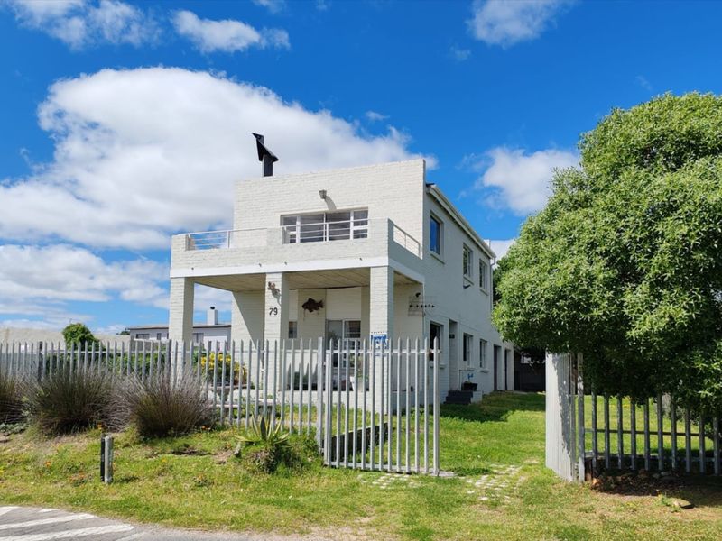 Front view of a two-story brick house featuring a balcony, metal security fencing, and a well-maintained garden area.