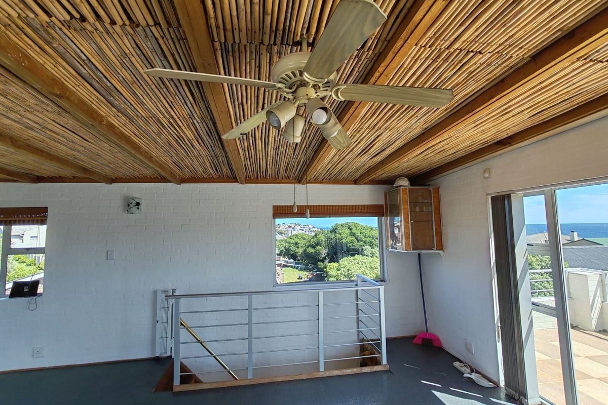 Spacious living area featuring a unique bamboo ceiling, ceiling fan, metal balustrade, and sliding doors leading to an outdoor balcony with scenic views.