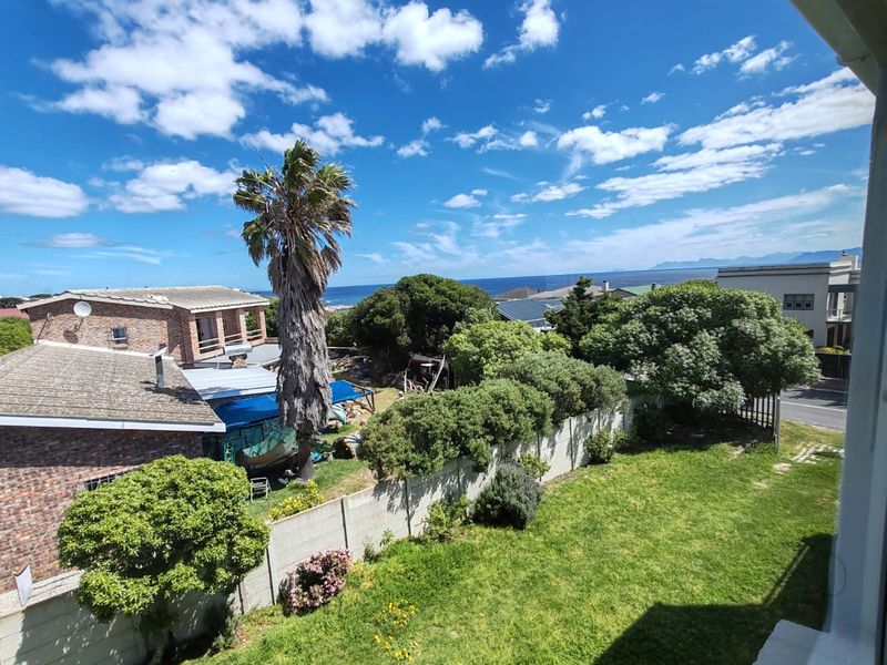 Elevated view overlooking a residential garden with mature trees, a precast boundary wall, and distant ocean views.