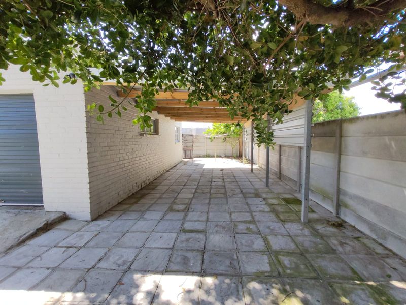 A paved outdoor patio area featuring a timber pergola structure, enclosed by a precast concrete boundary wall and adjacent to the garage.