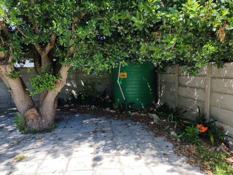 A private garden area featuring a large water storage tank, paved flooring, and a mature tree set against a precast concrete boundary wall.