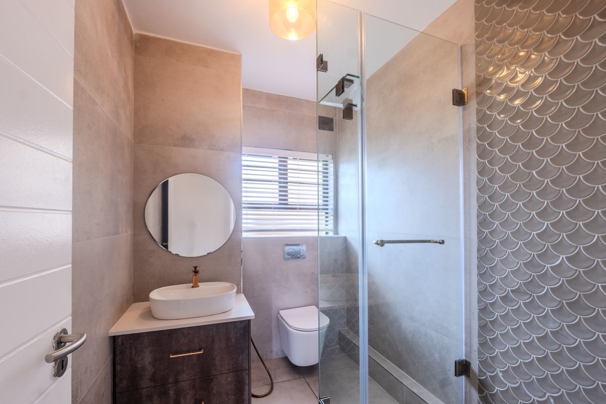 Modern bathroom featuring a sleek vanity with vessel sink, wall-mounted toilet, and a glass-enclosed shower with decorative scalloped feature tiling.