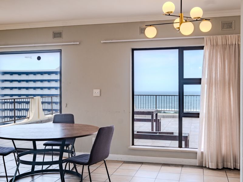Bright living area featuring tiled floors, modern lighting, and large sliding doors opening onto a balcony with ocean views.