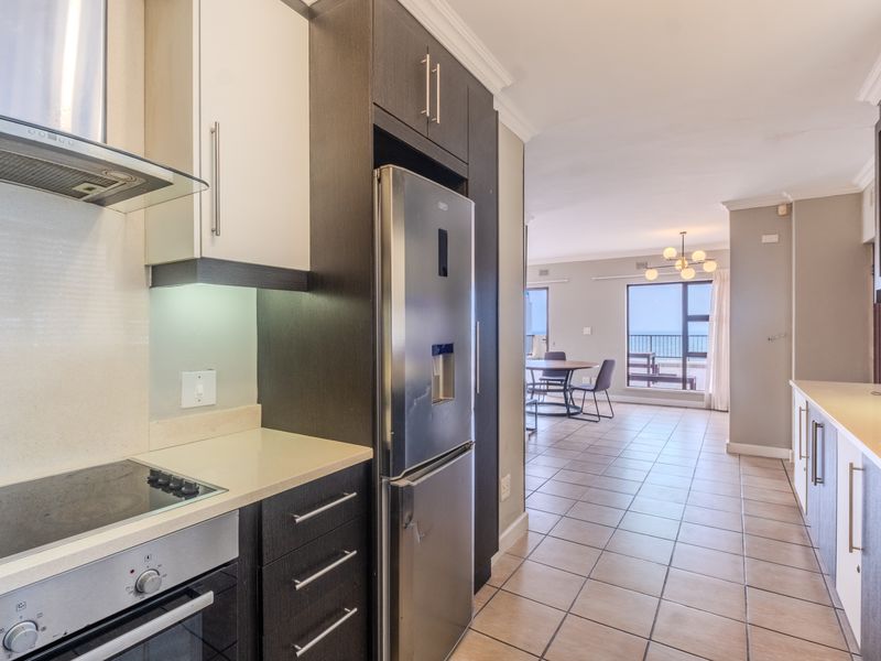 Modern open-plan kitchen featuring sleek dark and light cabinetry, stone countertops, and integrated appliances, flowing seamlessly into a bright living and dining area.