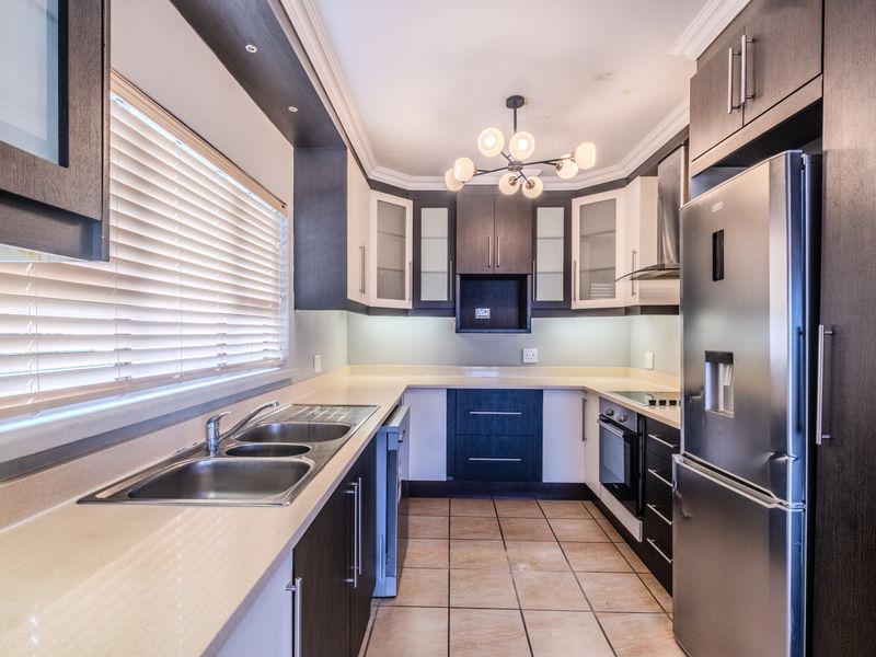 Modern kitchen featuring dark and light cabinetry, stone countertops, double basin sink, and integrated appliances with tiled flooring and ample natural light.