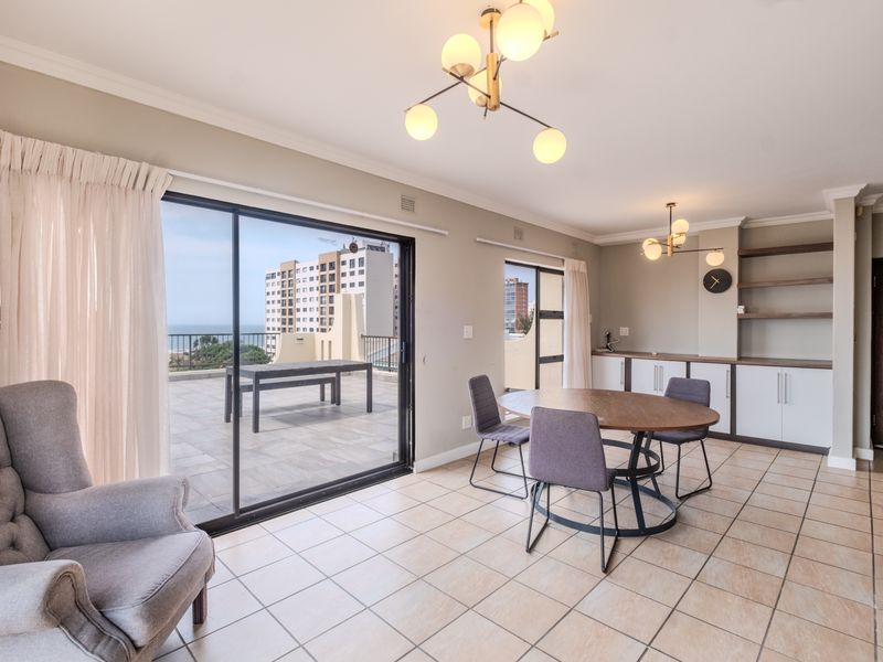Bright open-plan living and dining area featuring tiled floors, built-in cabinetry, and large sliding doors leading to a spacious balcony with coastal views.
