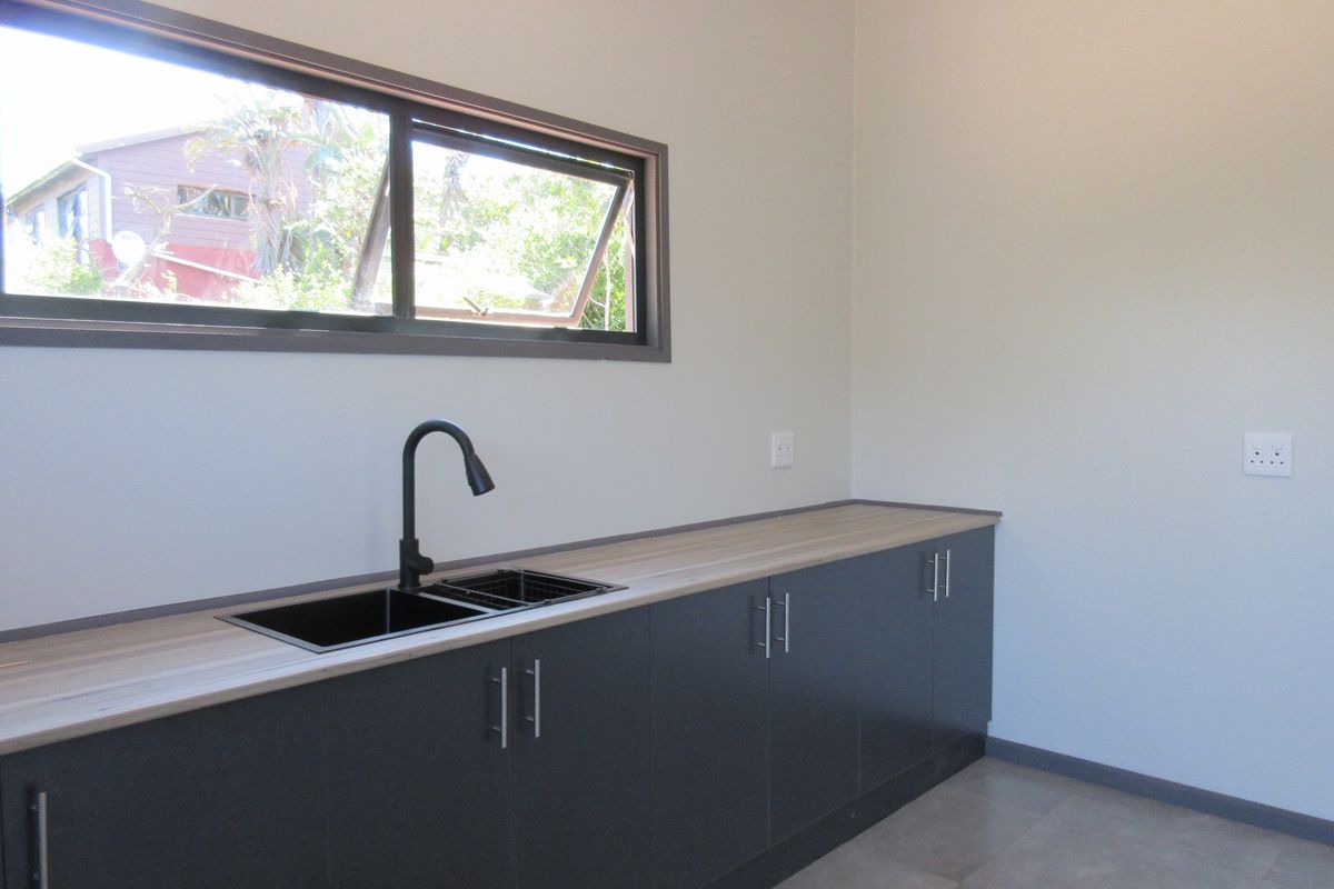A modern, minimalist kitchen area featuring dark grey cabinetry, a light wood-look laminate countertop, a black sink with matching faucet, and tiled flooring.