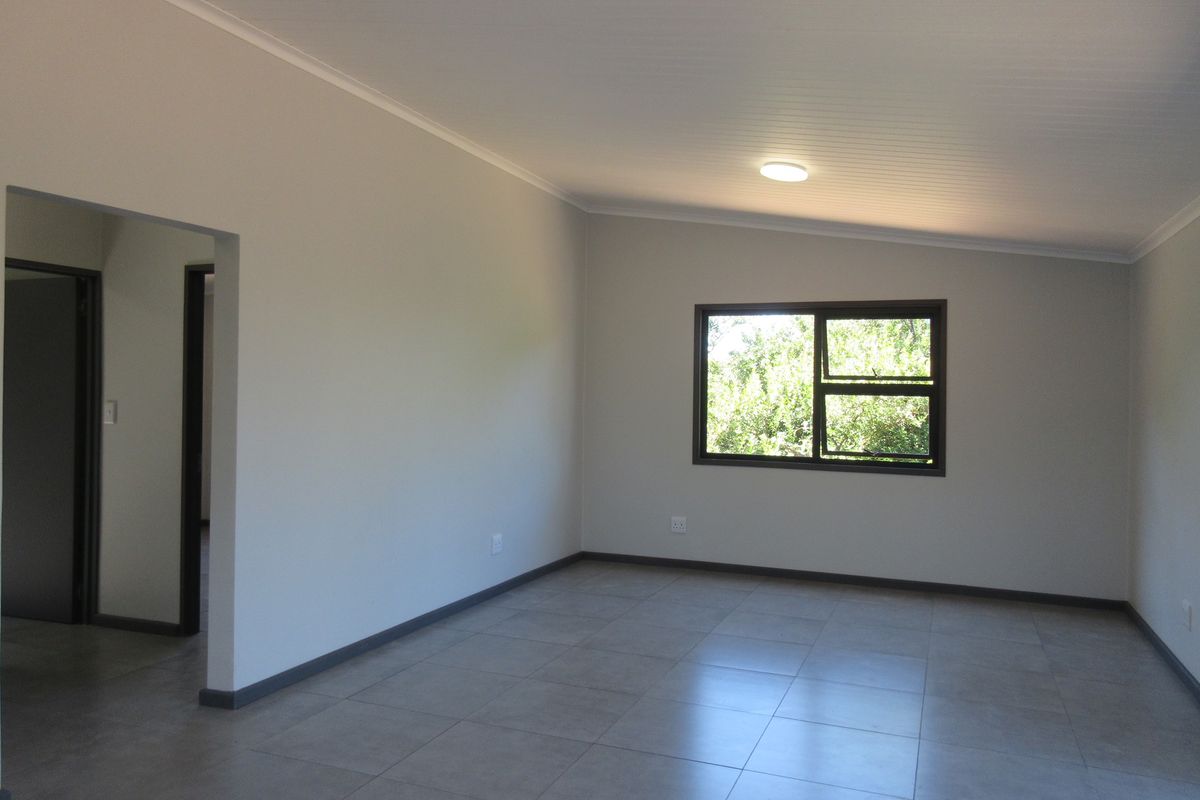 A bright, spacious, and empty living area featuring neutral wall tones, modern tiled flooring, and large aluminium-framed windows allowing for natural light.