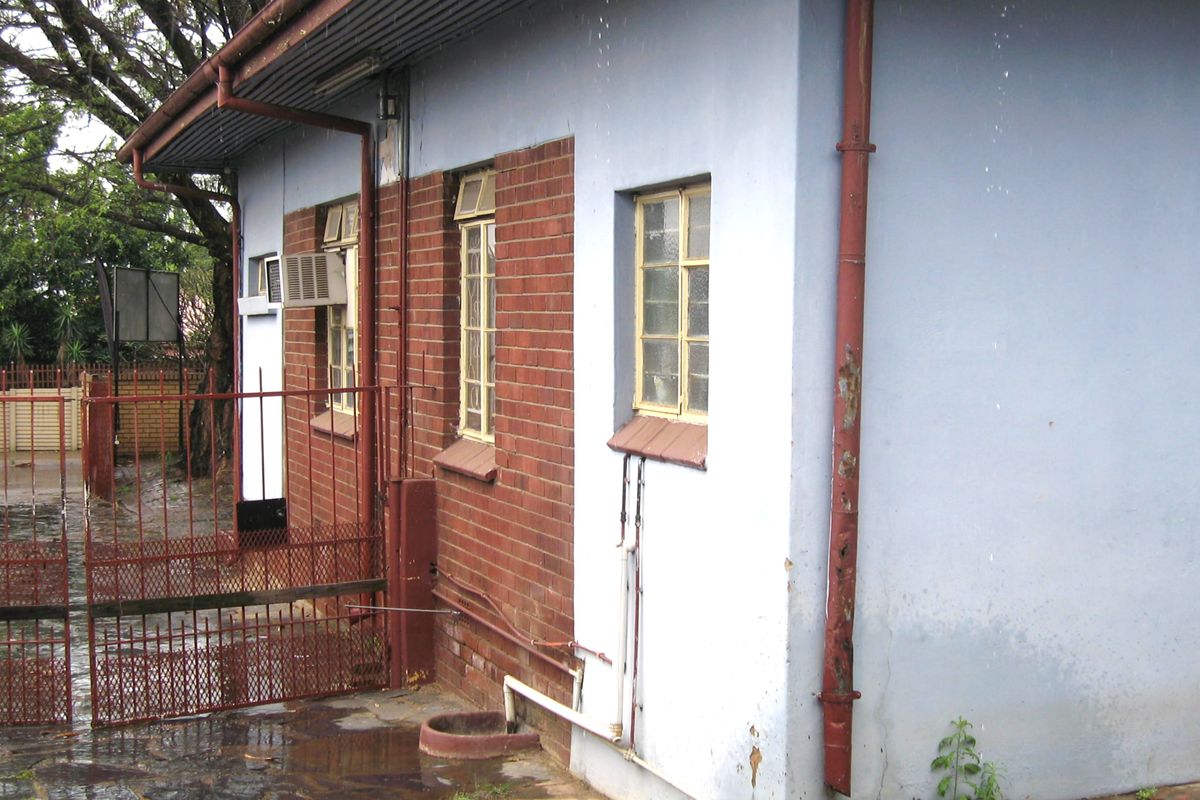 Rear exterior view of the property featuring brick and painted masonry walls, metal window frames, and a metal security gate.
