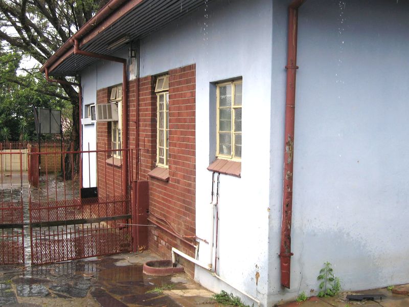 Rear exterior view of the property featuring brick and painted masonry walls, metal window frames, and a metal security gate.