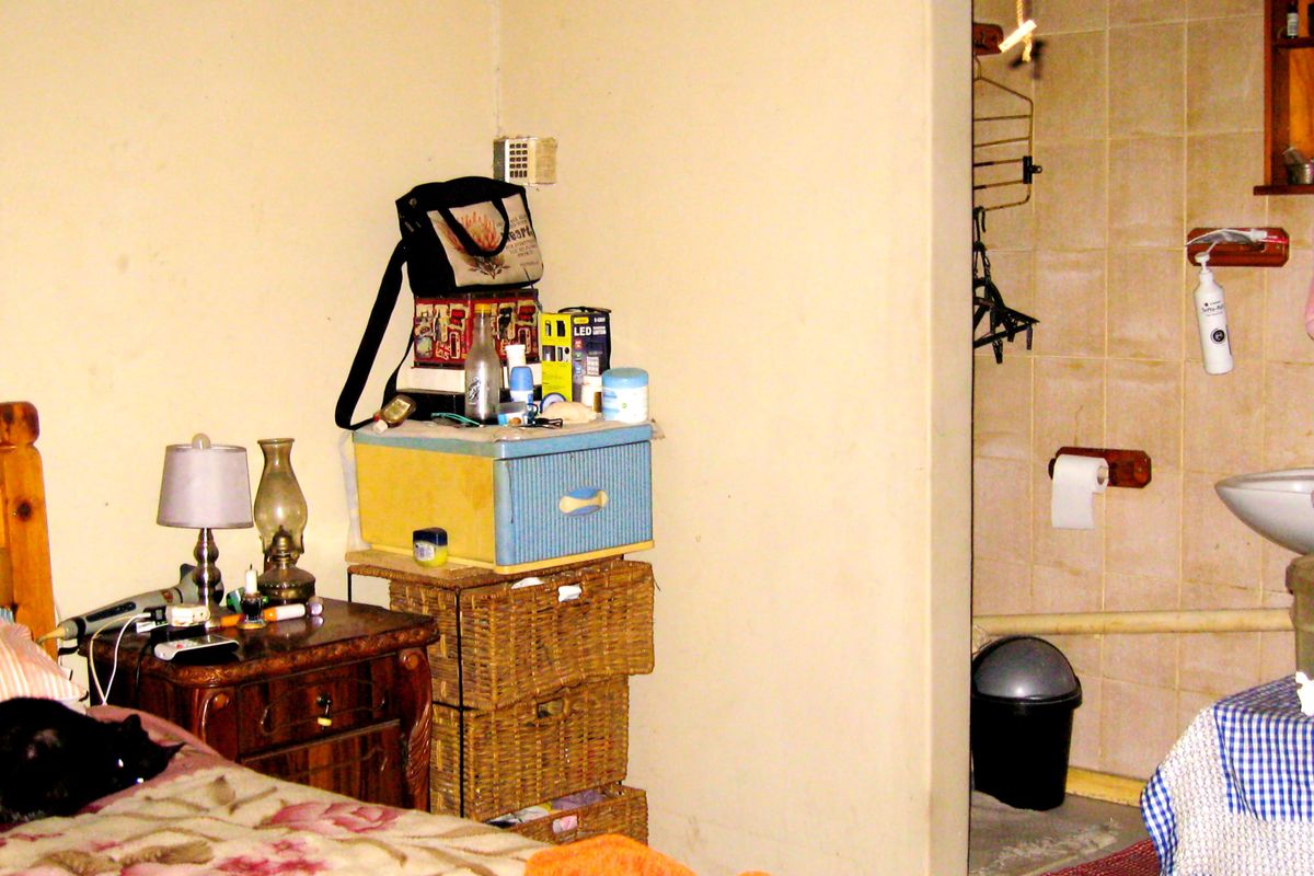 A bedroom with an adjoining bathroom area featuring tiled walls and a wall-mounted basin, requiring cosmetic updates to improve the overall finish.