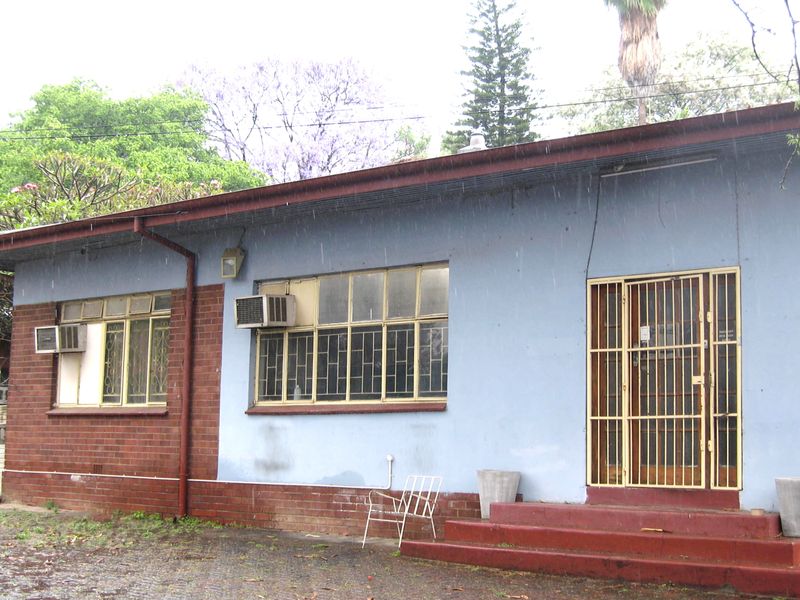Rear exterior view of the house featuring brick and painted wall finishes, security gates, and window-mounted air conditioning units.