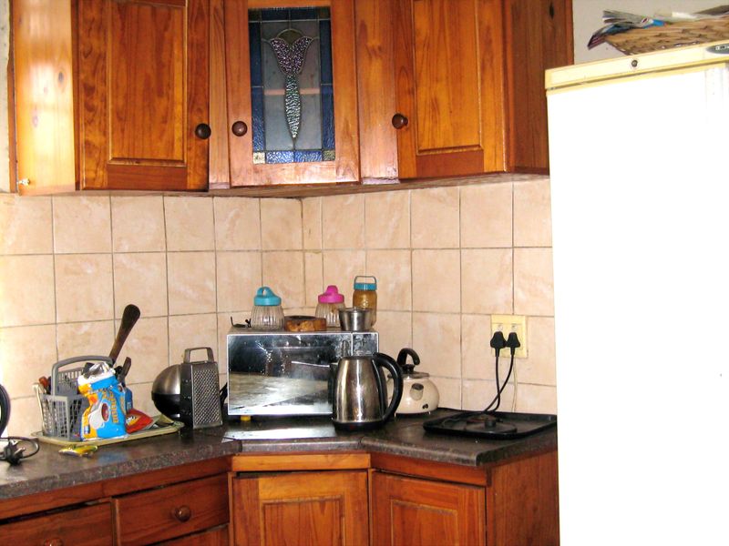 A dated kitchen area featuring traditional wooden cabinetry, tiled backsplash, and laminate countertops, offering potential for a modern renovation.