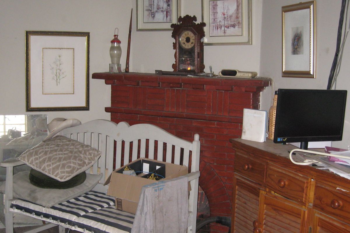 A living room area featuring a traditional red brick fireplace and mantel, showing signs of age and wear.