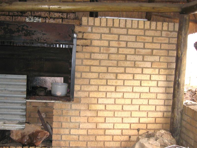Outdoor patio area featuring a built-in brick braai and traditional thatch roof structure with timber support poles.