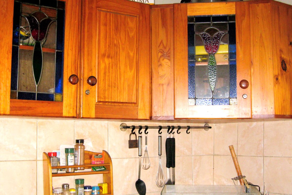A kitchen area featuring wooden wall-mounted cabinets with decorative stained glass inserts and ceramic wall tiling.