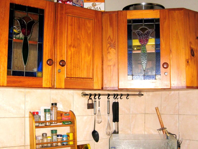 A kitchen area featuring wooden wall-mounted cabinets with decorative stained glass inserts and ceramic wall tiling.