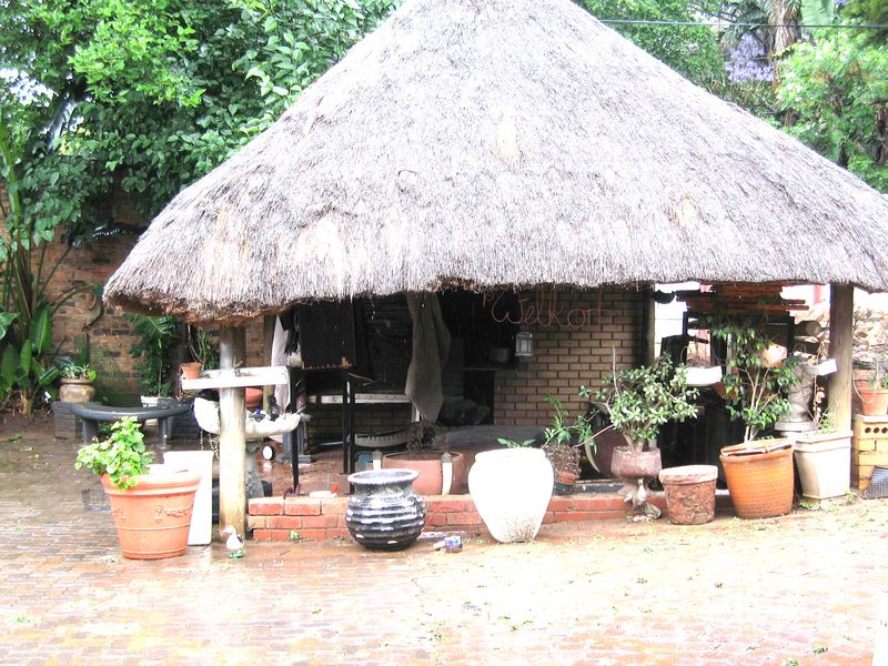 Outdoor thatched lapa area featuring brick construction and paved flooring, offering a rustic space for garden entertainment.