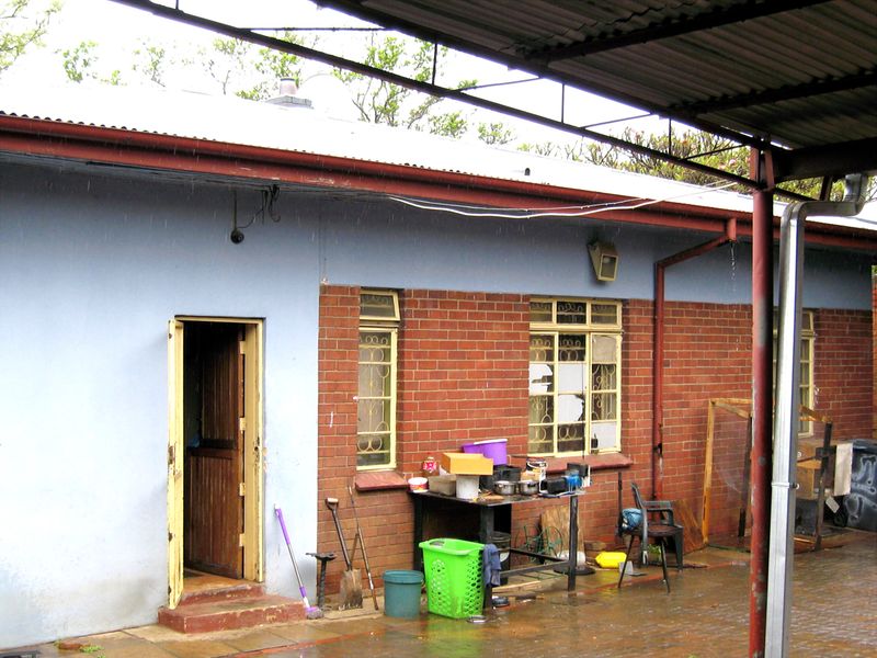 Rear exterior view of the property featuring a covered patio area, brick and plaster facade, and security-barred windows in need of maintenance.