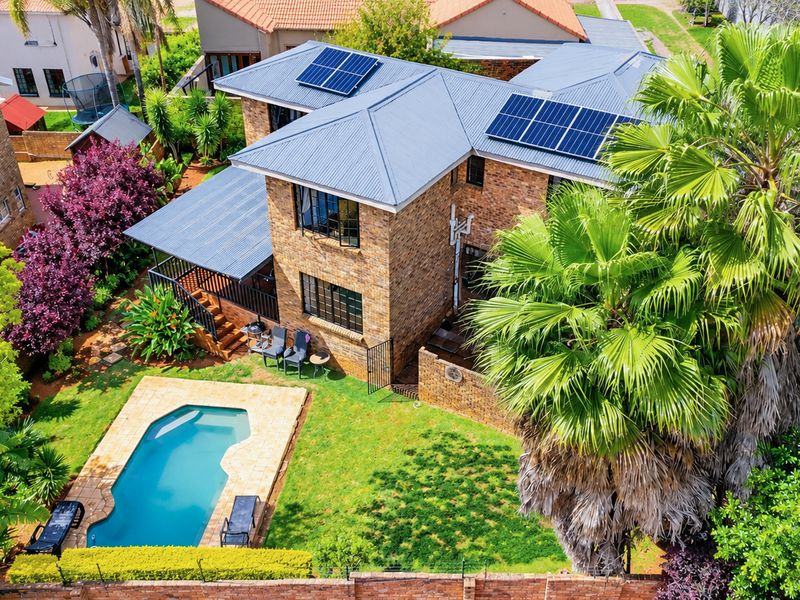 Aerial view of a two-story brick house featuring a metal roof with solar panels, a swimming pool, and a well-maintained garden.