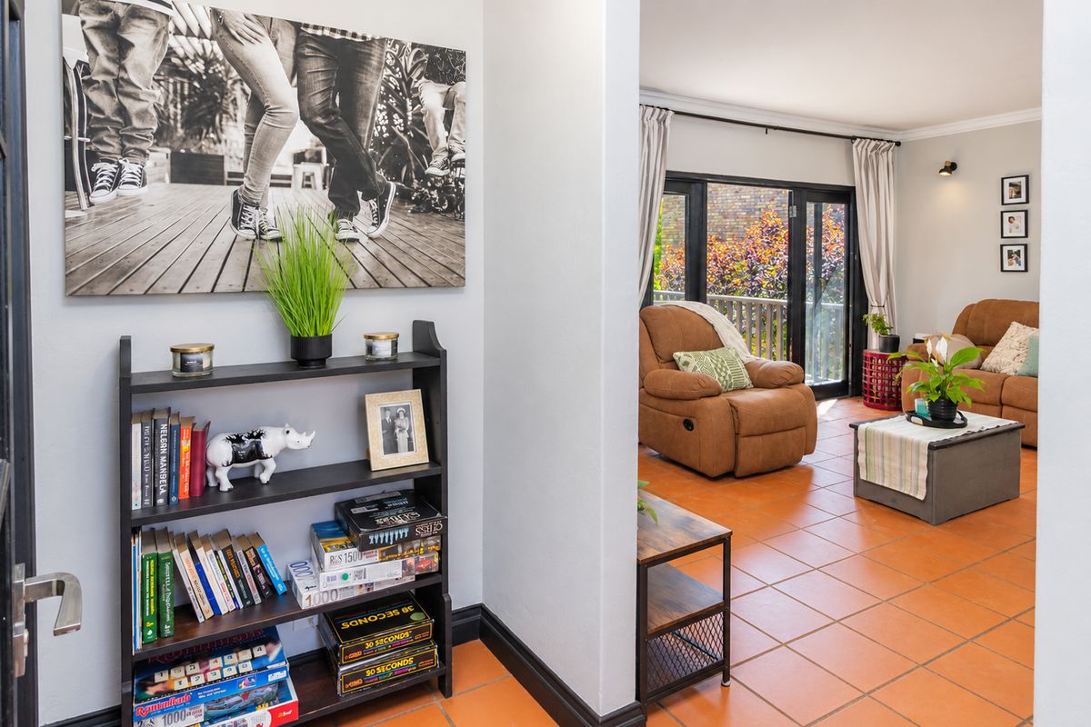 A view from a hallway into a living room featuring terracotta floor tiles and sliding glass doors leading to an outdoor area.