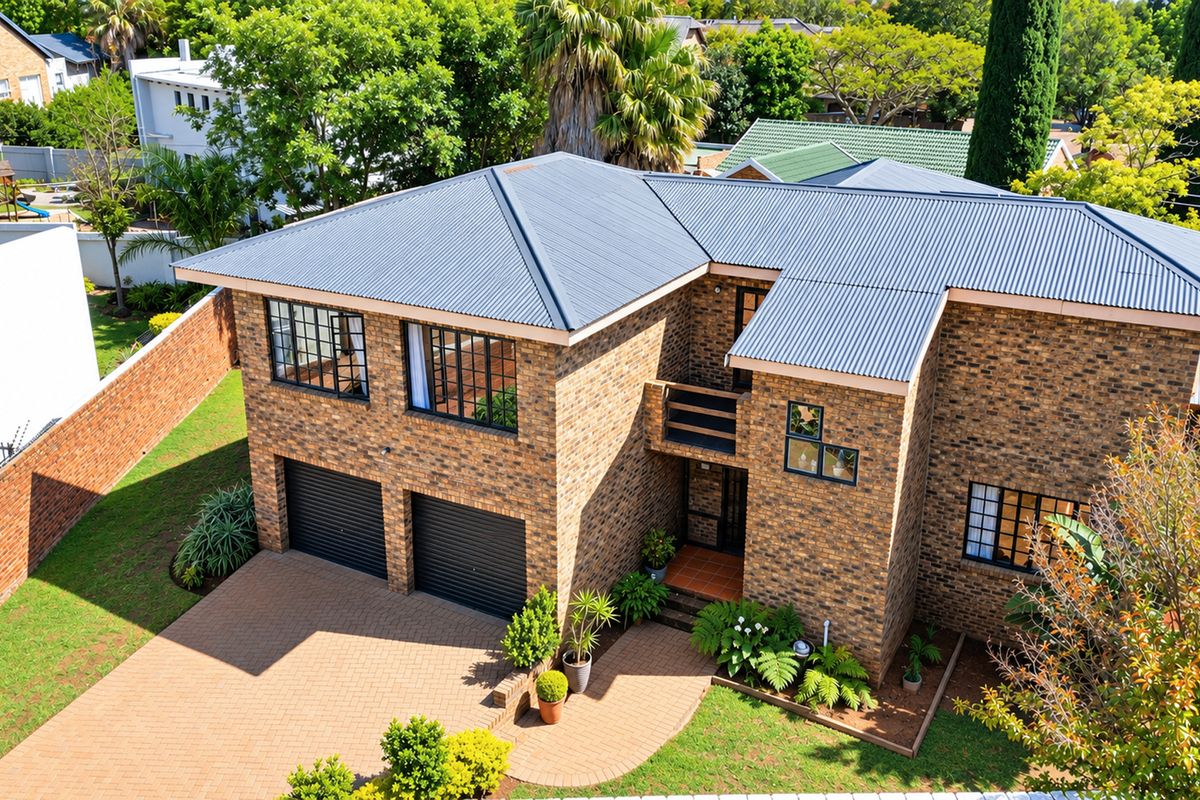 Aerial view of a double-story face brick house featuring a corrugated metal roof, double garage, and paved driveway in a suburban setting.