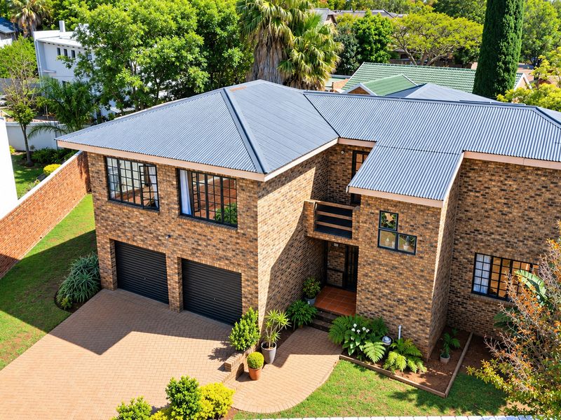 Aerial view of a double-story face brick house featuring a corrugated metal roof, double garage, and paved driveway in a suburban setting.