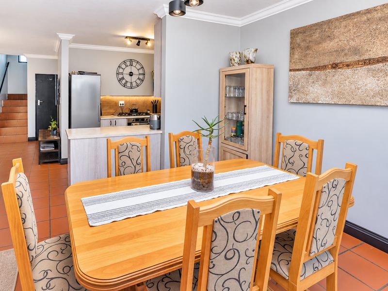 Open-plan dining area featuring tiled flooring and coving, seamlessly connected to a functional kitchen space with built-in cabinetry and a stovetop.