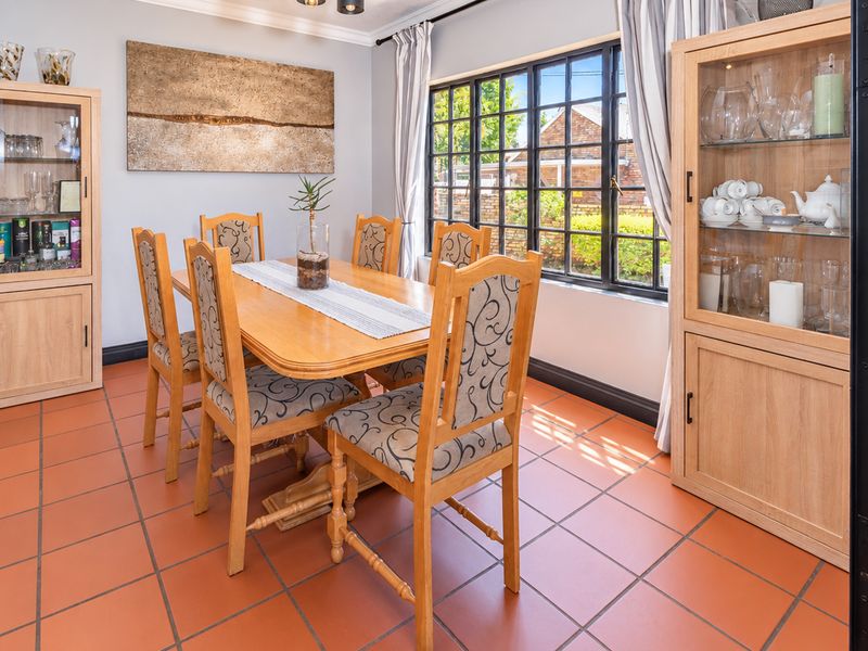 A well-lit dining room featuring terracotta floor tiles and a large black-framed window, providing a bright and functional space for family meals.