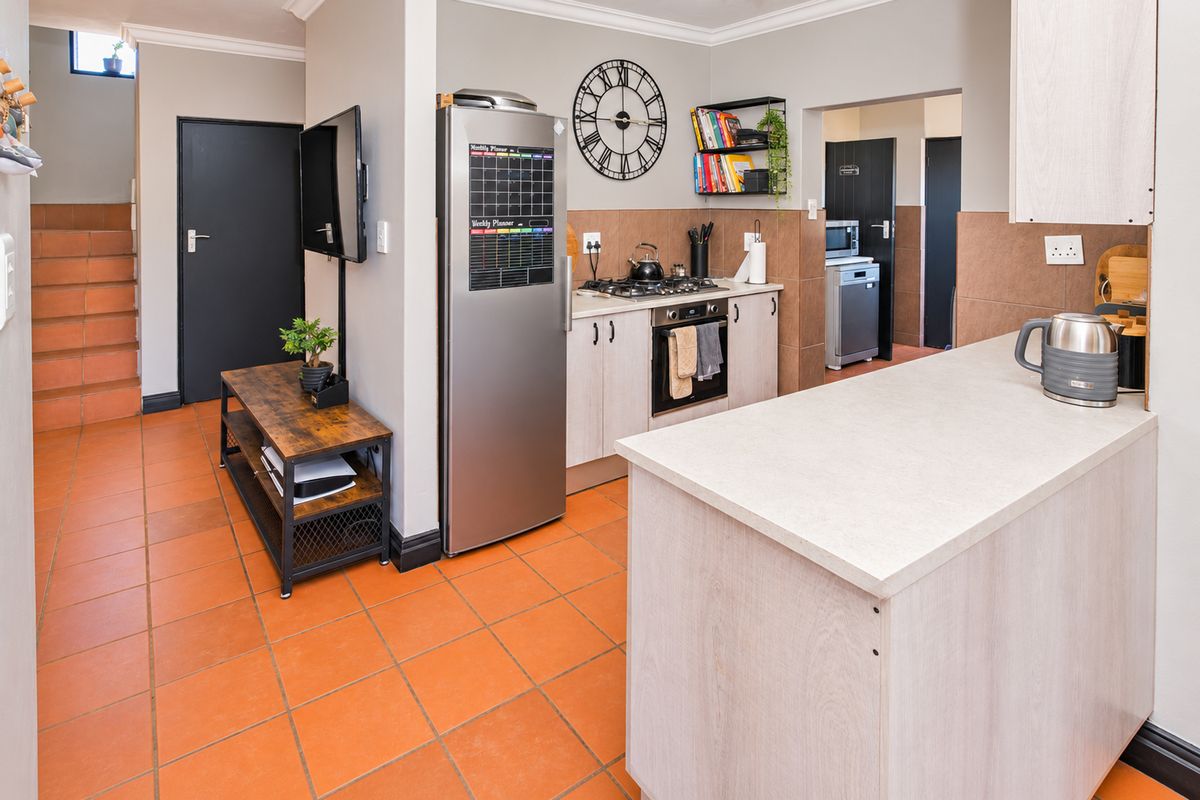A functional kitchen featuring built-in cabinetry, gas hob, oven, and tiled flooring, with an adjacent staircase and access to a secondary utility area.