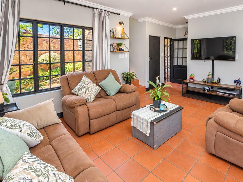 A comfortable living room featuring terracotta floor tiles, black metal-framed windows, and neutral wall finishes, providing a bright and inviting space.