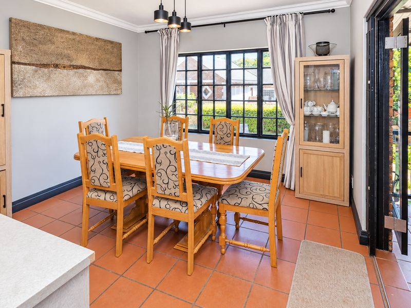 A well-lit dining room featuring terracotta floor tiles, black-framed windows, and built-in cabinetry, offering a functional space for family meals and entertaining.