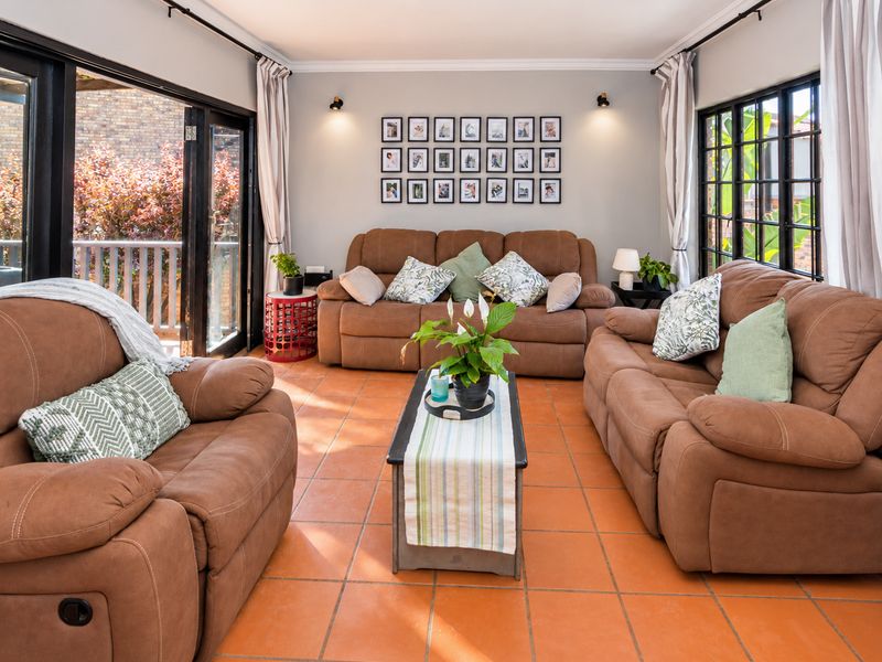 A bright and inviting living room featuring terracotta floor tiles, large black-framed glass sliding doors, and ample natural light.