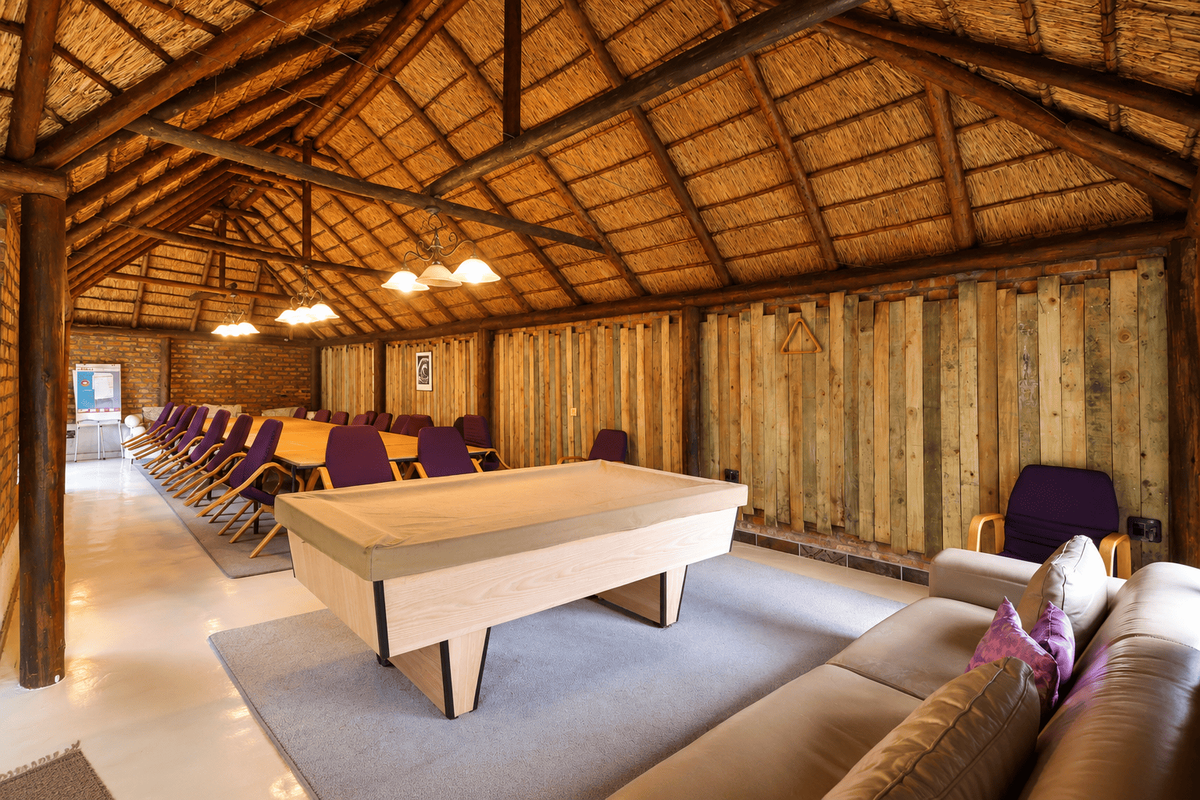 Spacious entertainment area featuring a high vaulted thatched roof with exposed timber trusses, rustic timber wall paneling, and polished concrete floors.
