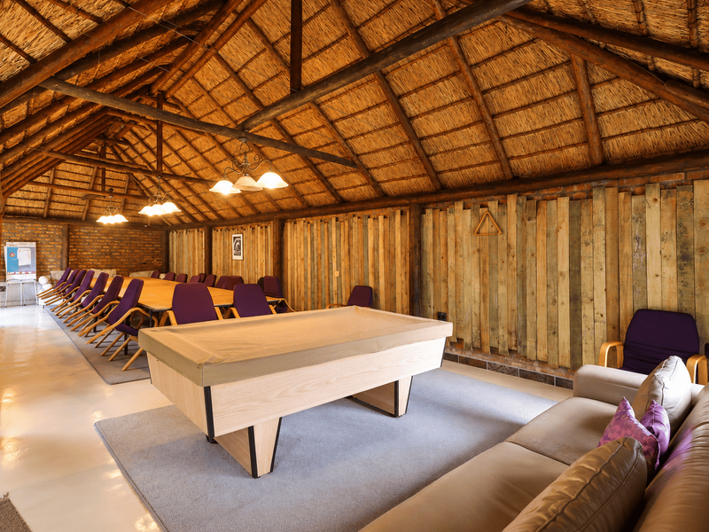 Spacious entertainment area featuring a high vaulted thatched roof with exposed timber trusses, rustic timber wall paneling, and polished concrete floors.