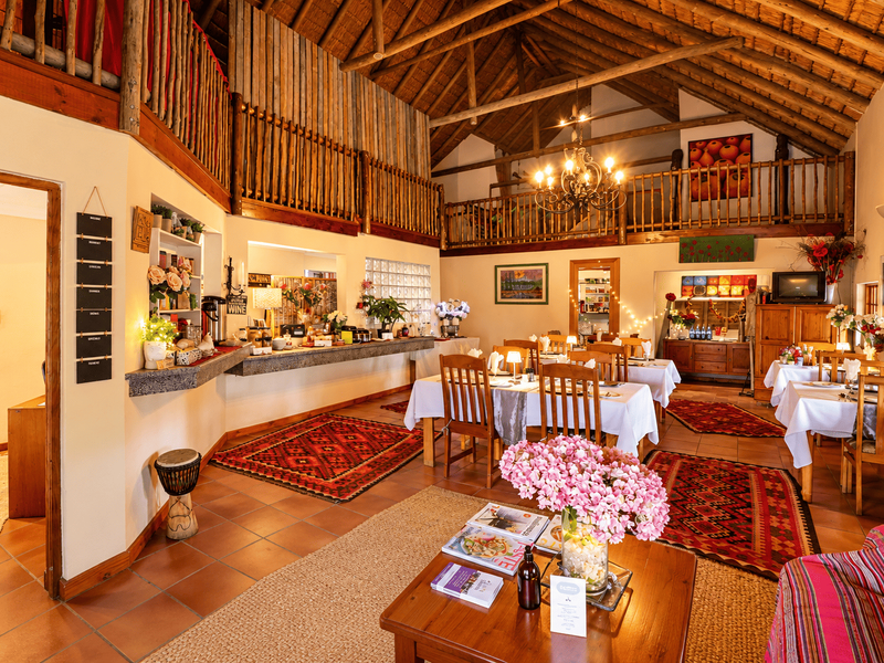 Spacious open-plan dining and living area featuring a high thatched roof with exposed timber trusses, a mezzanine level, and rustic tiled flooring.