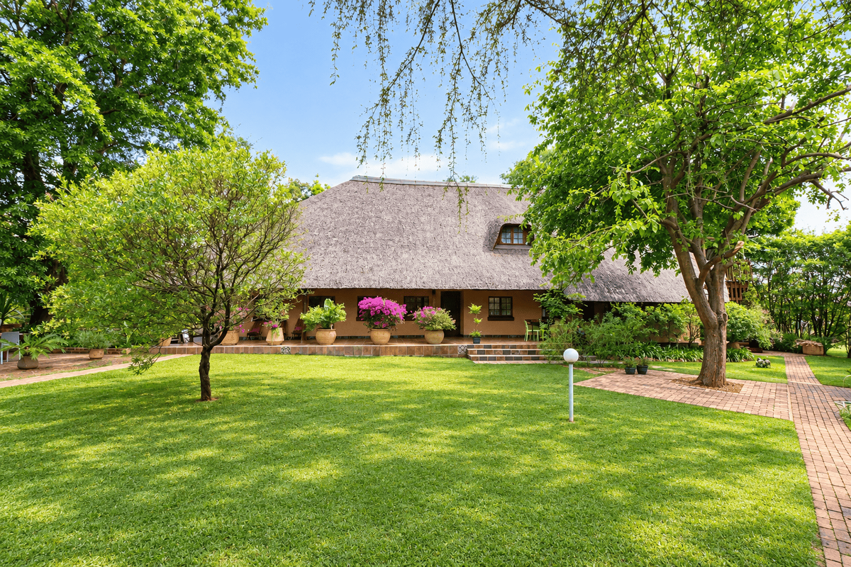 A well-maintained rear garden view featuring a traditional thatched roof house with a tiled patio and established landscaping.